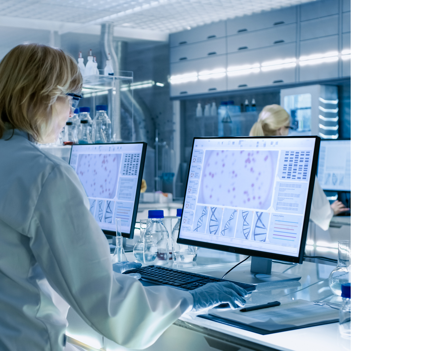 Eine Biologin steht im Labor und bedient einen Computer auf dem DNA Strukturen zu sehen sind