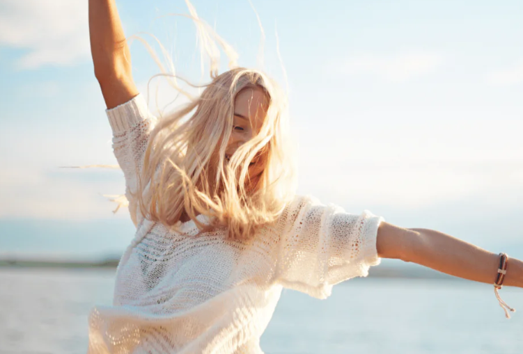 young blonde woman dancing by the water on a sunny day